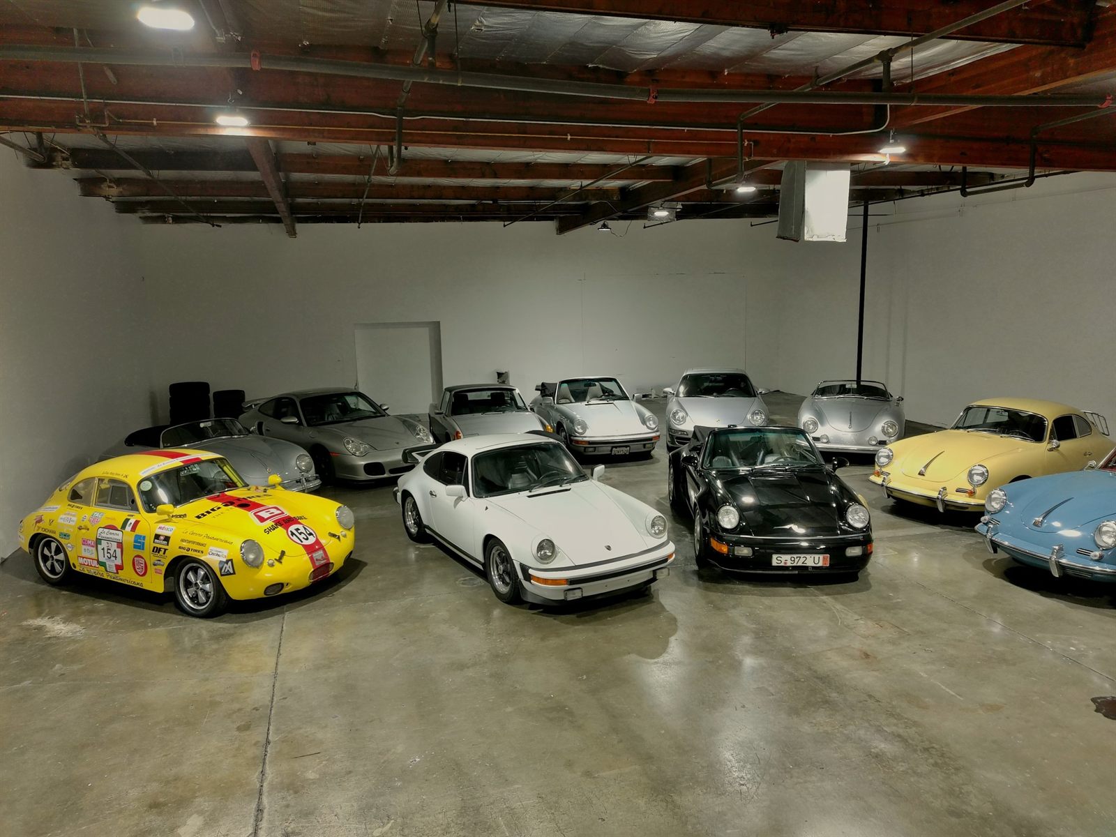 Garage full of classic Porsches, with a yellow racing-livery 911 up front