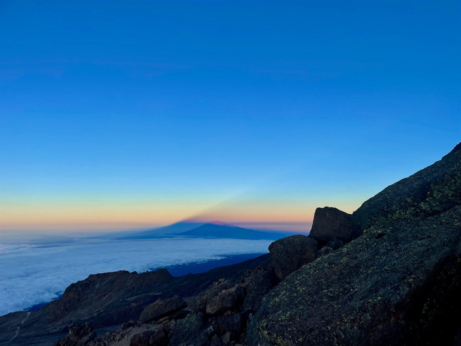 A mountain's shadow cast across a sea of clouds at dusk, seen from the summit