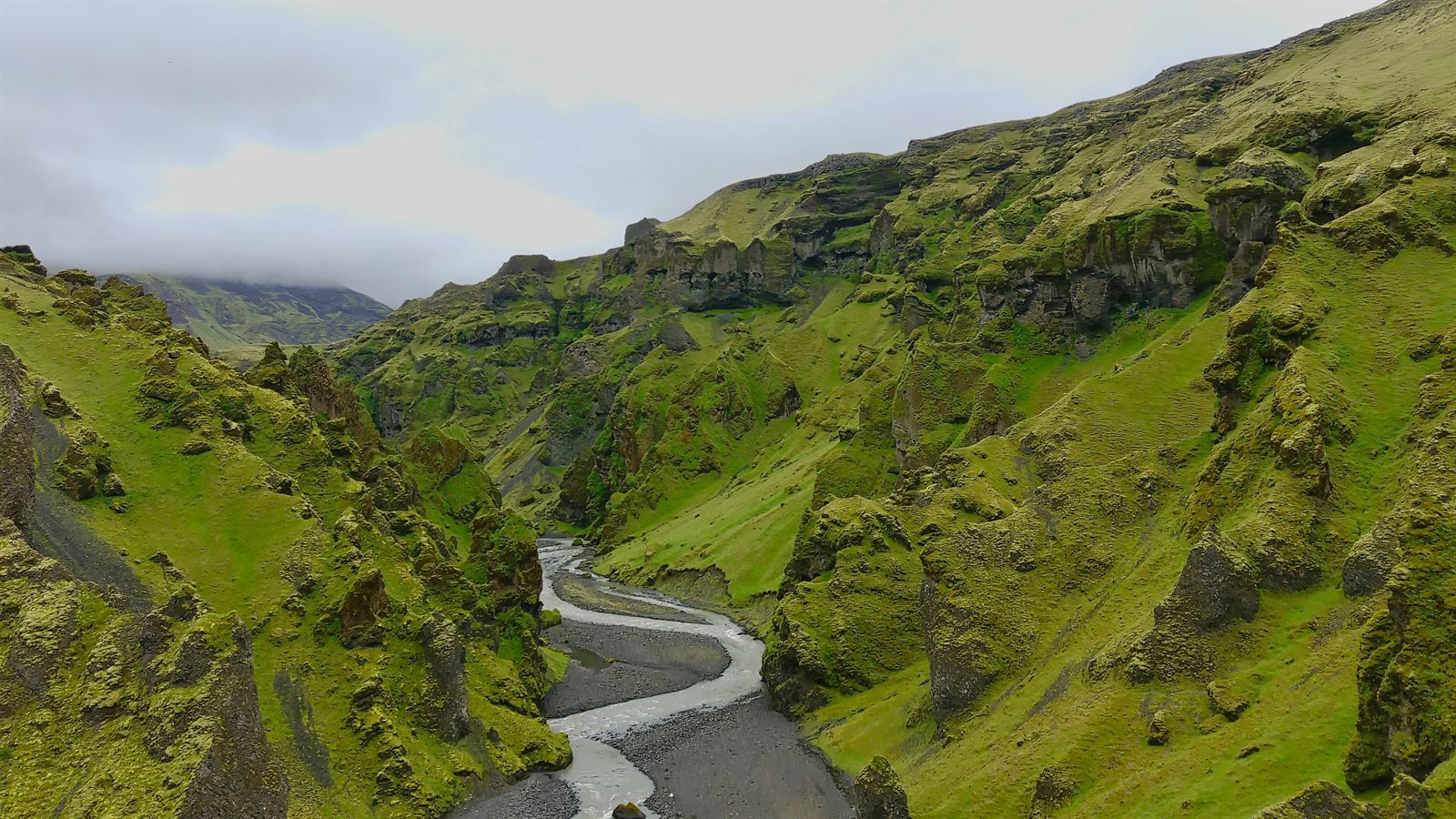 Braided glacial river threading a mossy green canyon in the Icelandic highlands