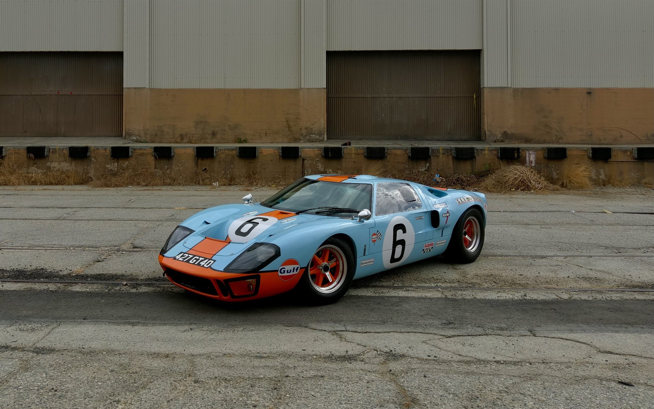 A Gulf-livery Ford GT40 in light blue and orange parked outside an industrial warehouse