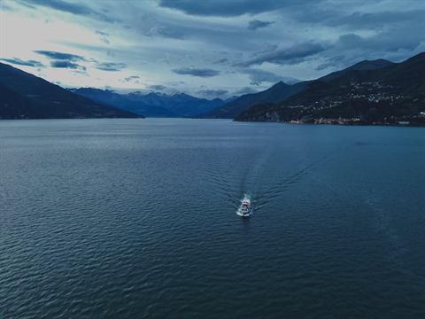 Boat crossing a dark alpine lake at dusk, mountains fading into the haze