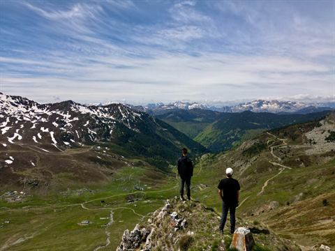 Two hikers on a rocky overlook above a sweeping green alpine valley