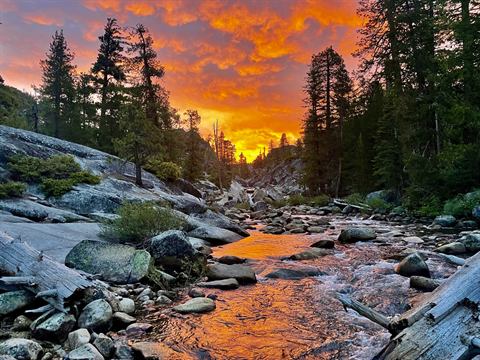 Fiery sunset sky over a boulder-strewn mountain creek