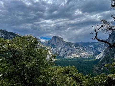 Half Dome in the distance under a dramatic sky of storm clouds