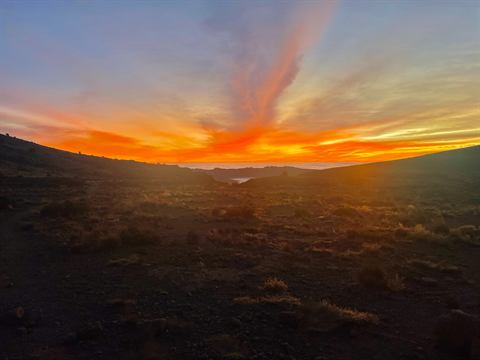 Burnt-orange sunset over a dark ridgeline and distant water