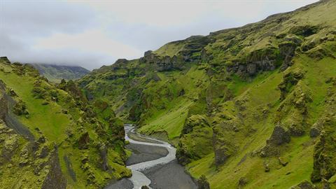 Braided glacial river threading a mossy green canyon in the Icelandic highlands