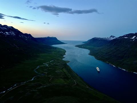 Ship steaming up a still Icelandic fjord between dark mountains at dusk